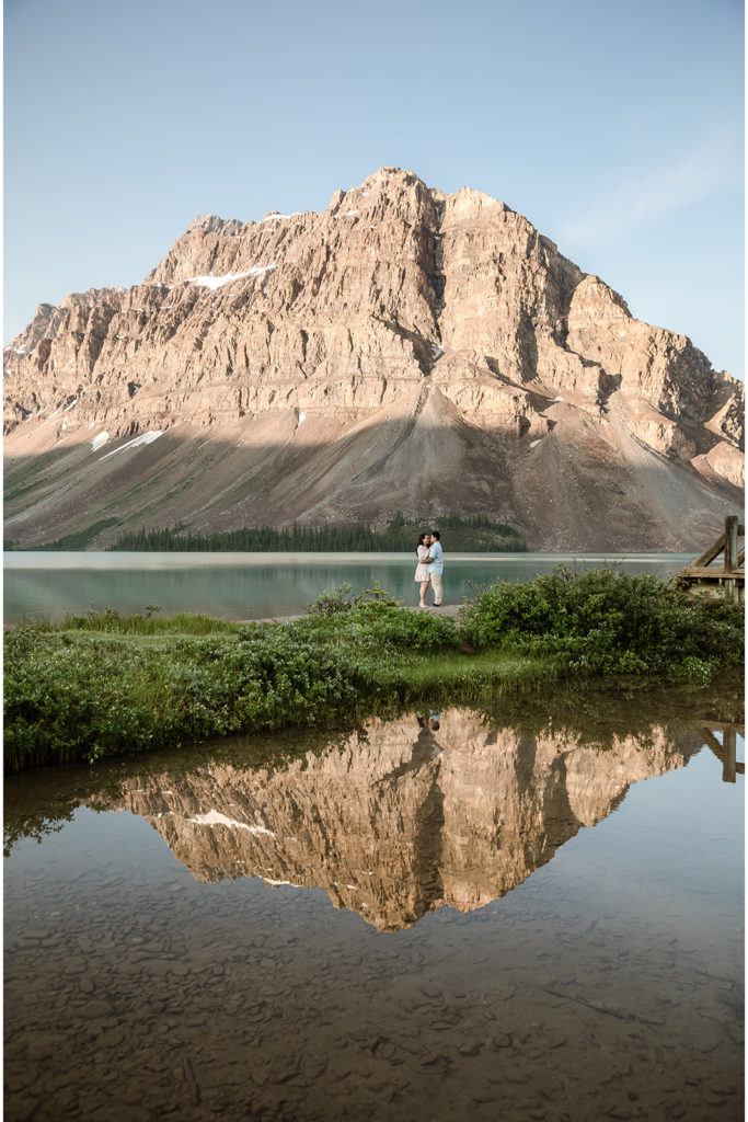 A couple standing in front of a lake in Banff during sunrise.