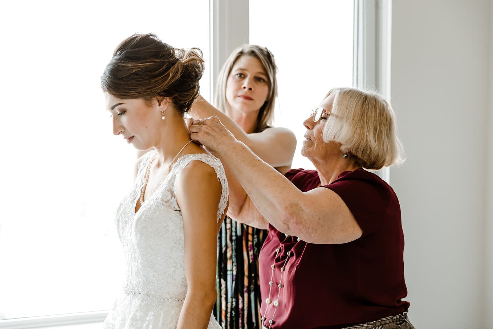 A bride including her family in her elopement by having her grandmother helping to put on her neckless, with the bride's mother in the background