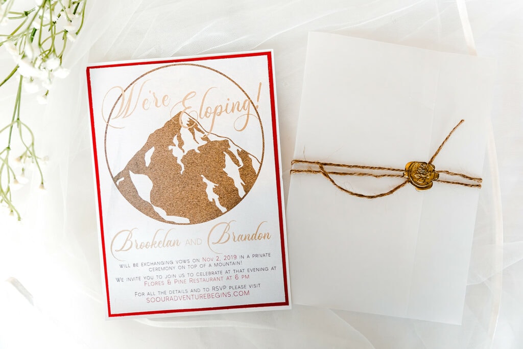 A picture of a card titled "We're Eloping!" beside a white envelope with a gold wax seal, to be sent from a couple to their friends and family. 