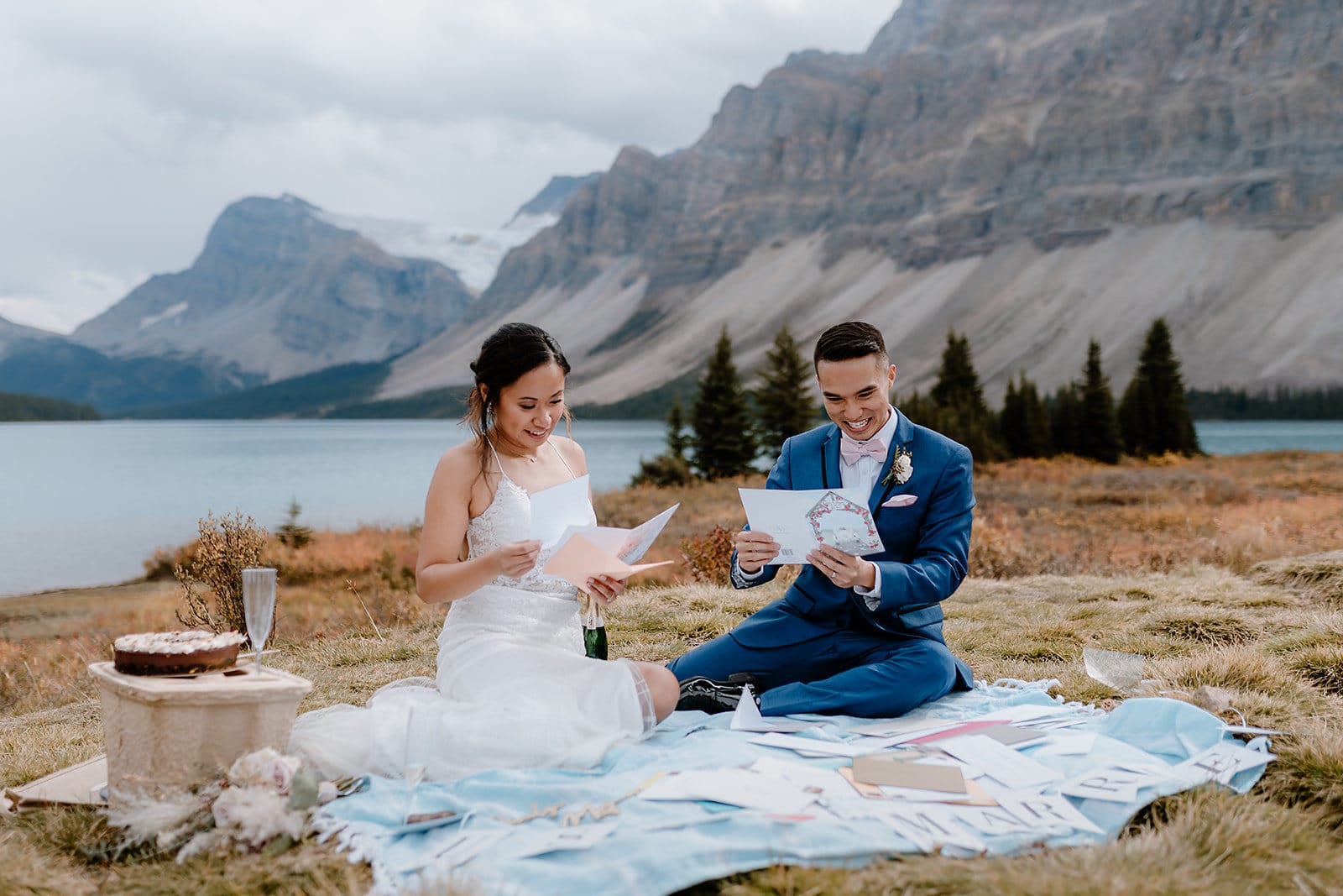 A bride and groom including their friends and family in their elopement by reading letters written to them while having a picnic in front of Bow lake in Banff Alberta