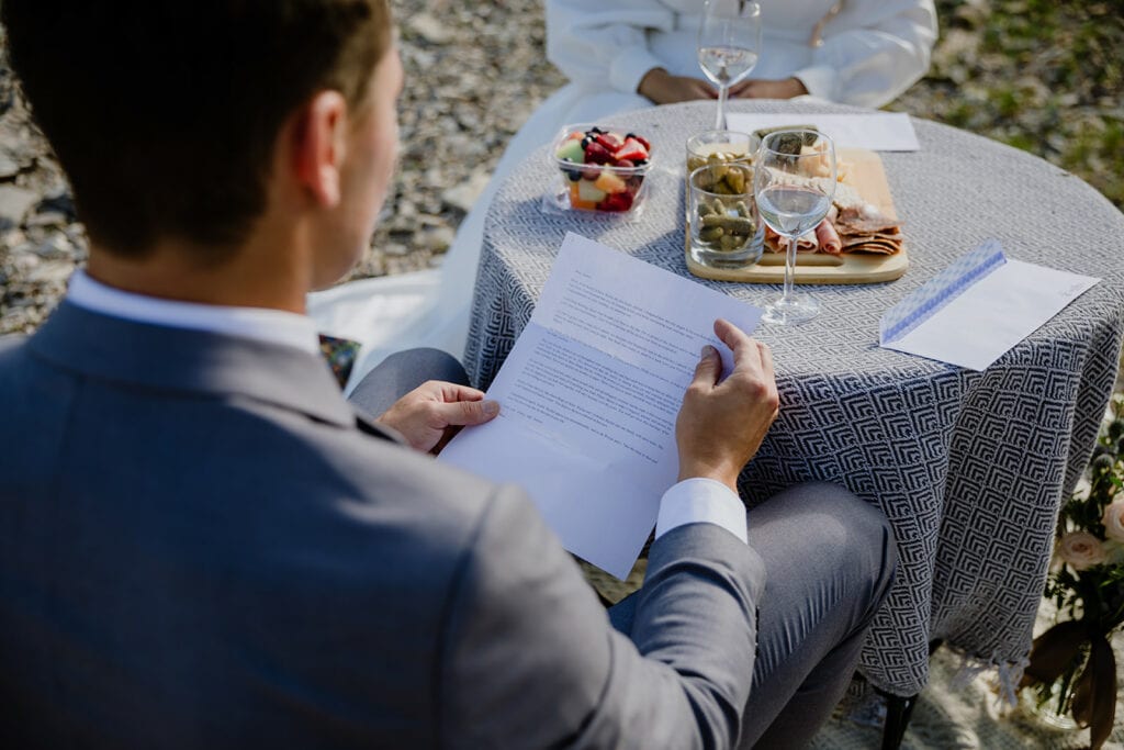 A groom facing away from the camera reading a letter written by his family to his bride on their elopement day.
