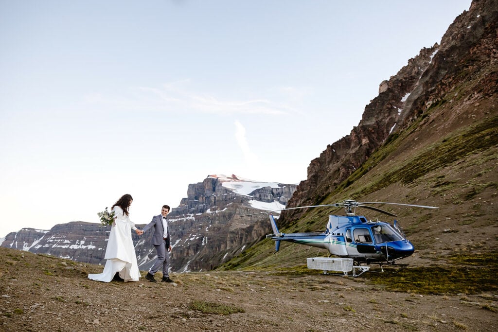 Bride and groom walking towards a helicopter in Banff surrounded by mountains.