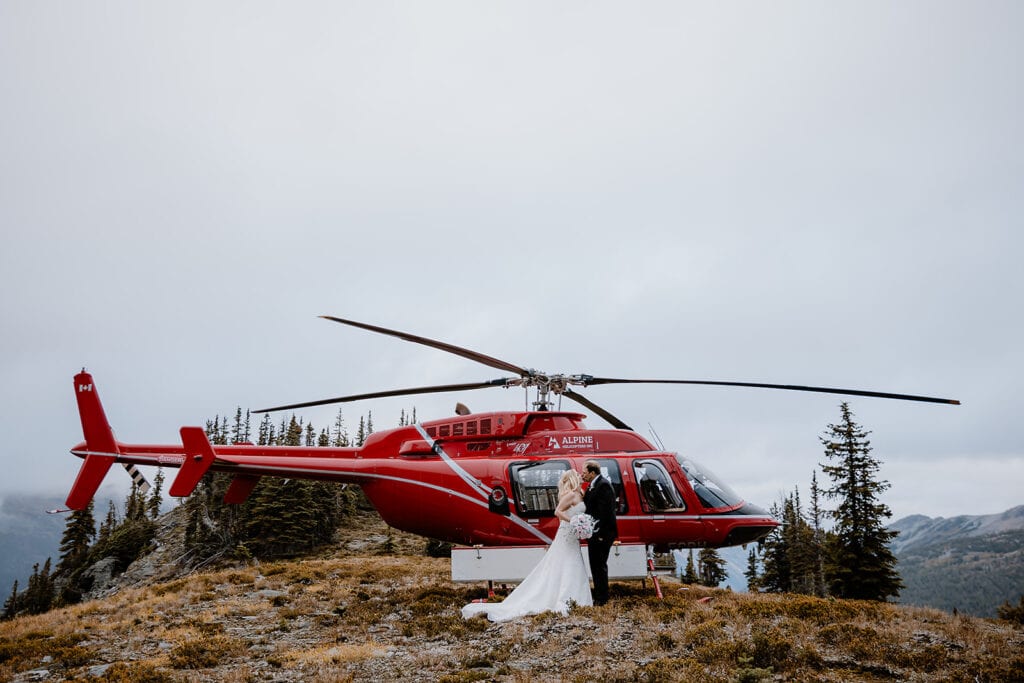 Couple kissing by a helicopter on their wedding day in Banff