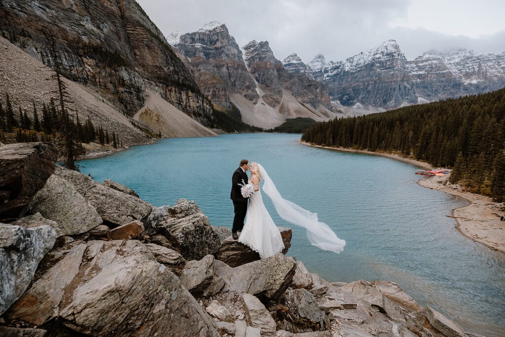 A couple kissing on their helicopter elopement, and the bride's veil is floating in the wind 