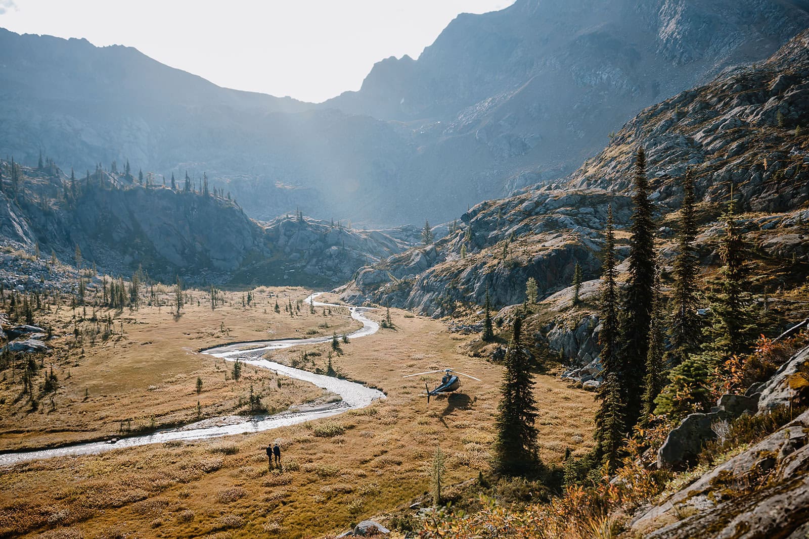 Helicopter landed on a field beside a winding river on a valley of Canadian Rockies 