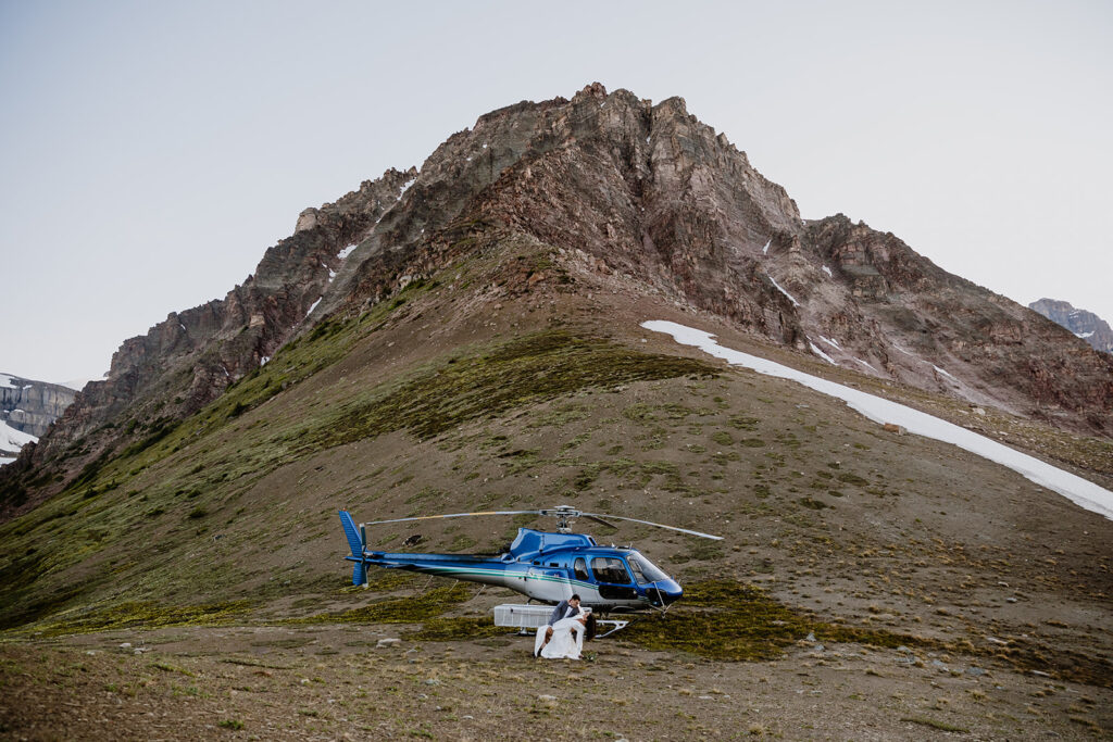 Groom dipping his bride in front of a helicopter with a mountain behind them on their elopement day in Banff