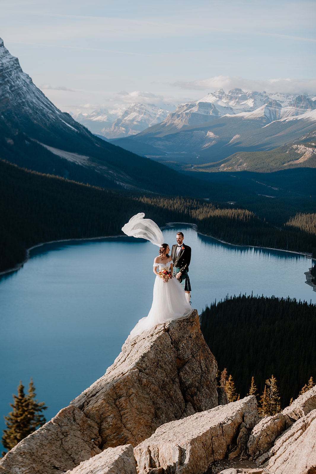 a bride's veil is blowing in the wind while standing on the rocks above Peyto Lake 