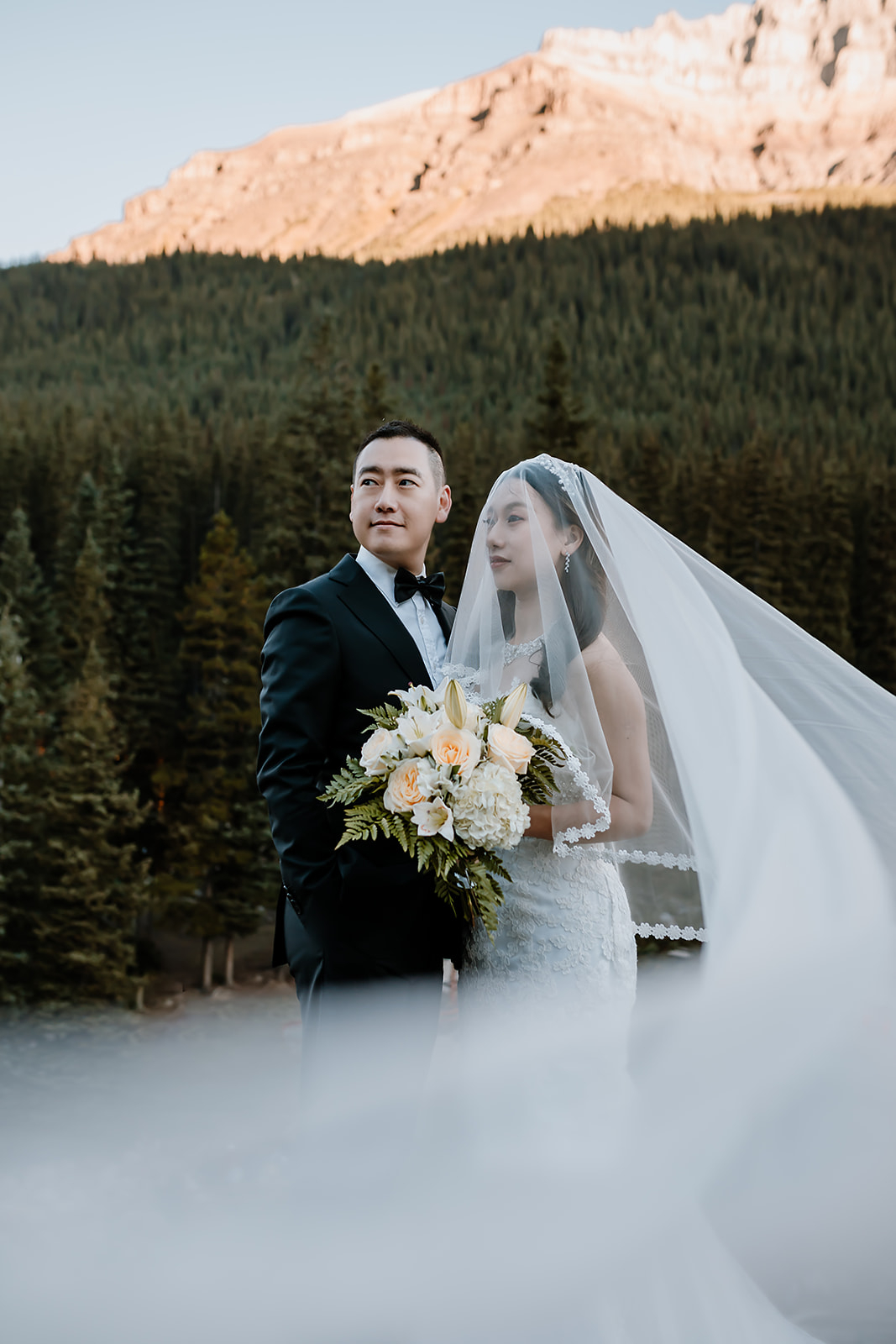 bride and groom standing together with the brides veil wrapped around them 