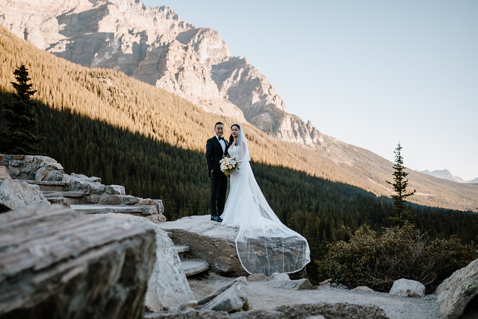a bride and groom standing on the rockpile during their pre-wedding canoe ride photoshoot at Moraine Lake 