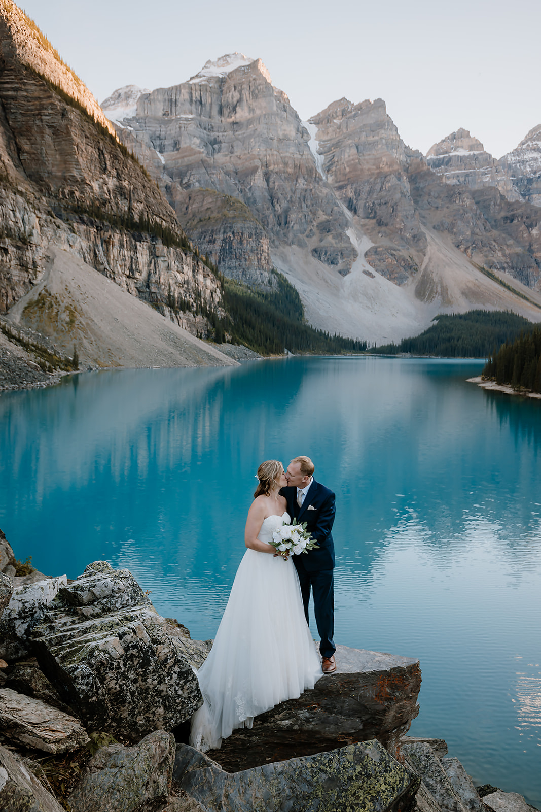 get-married-in-Banff a bride and groom kissing on their wedding day with a stunning blue glacier lake behind them
