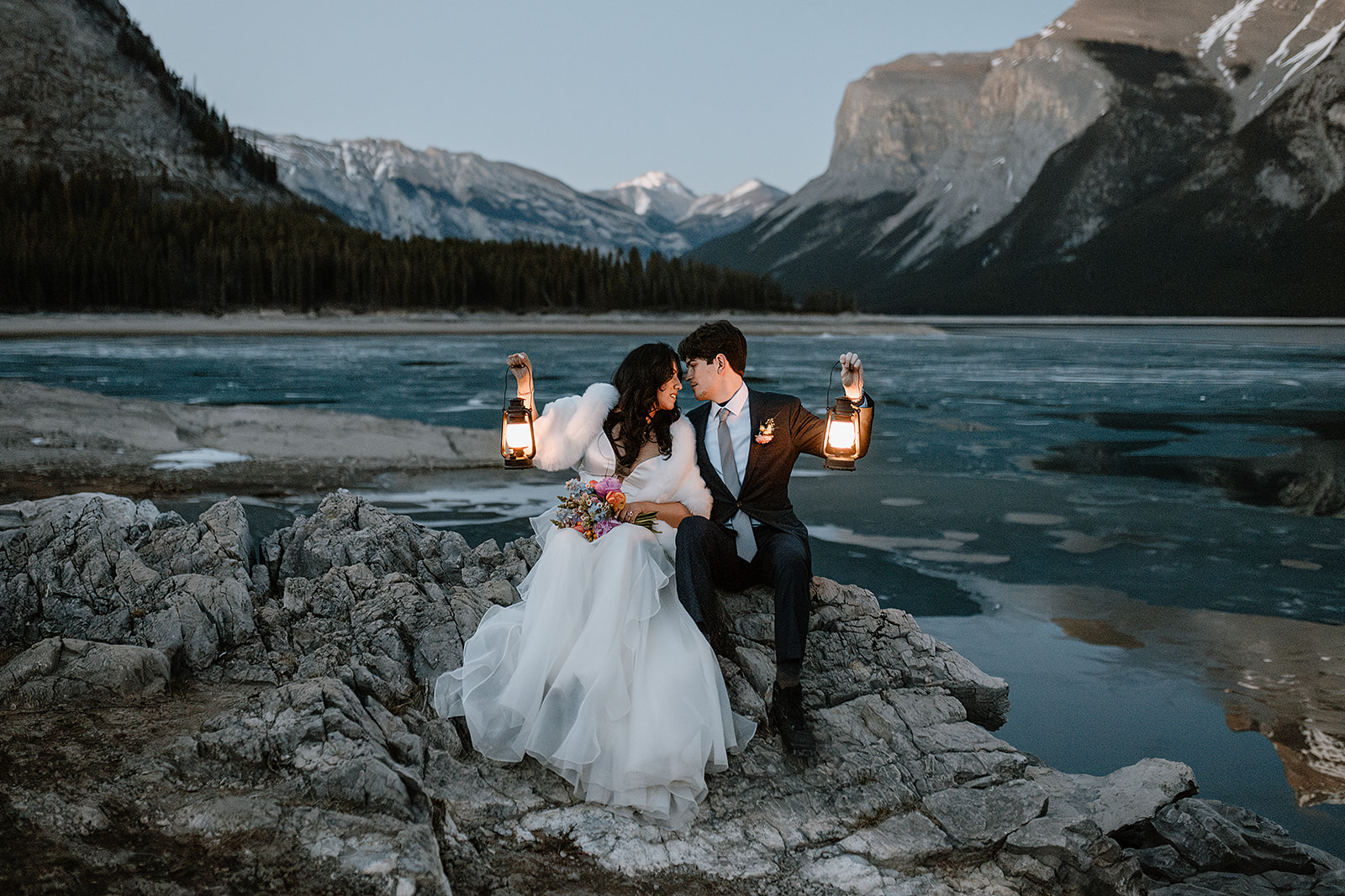 get-married-in-Banff bride and groom sitting my a frozen mountain lake while they get married in Banff