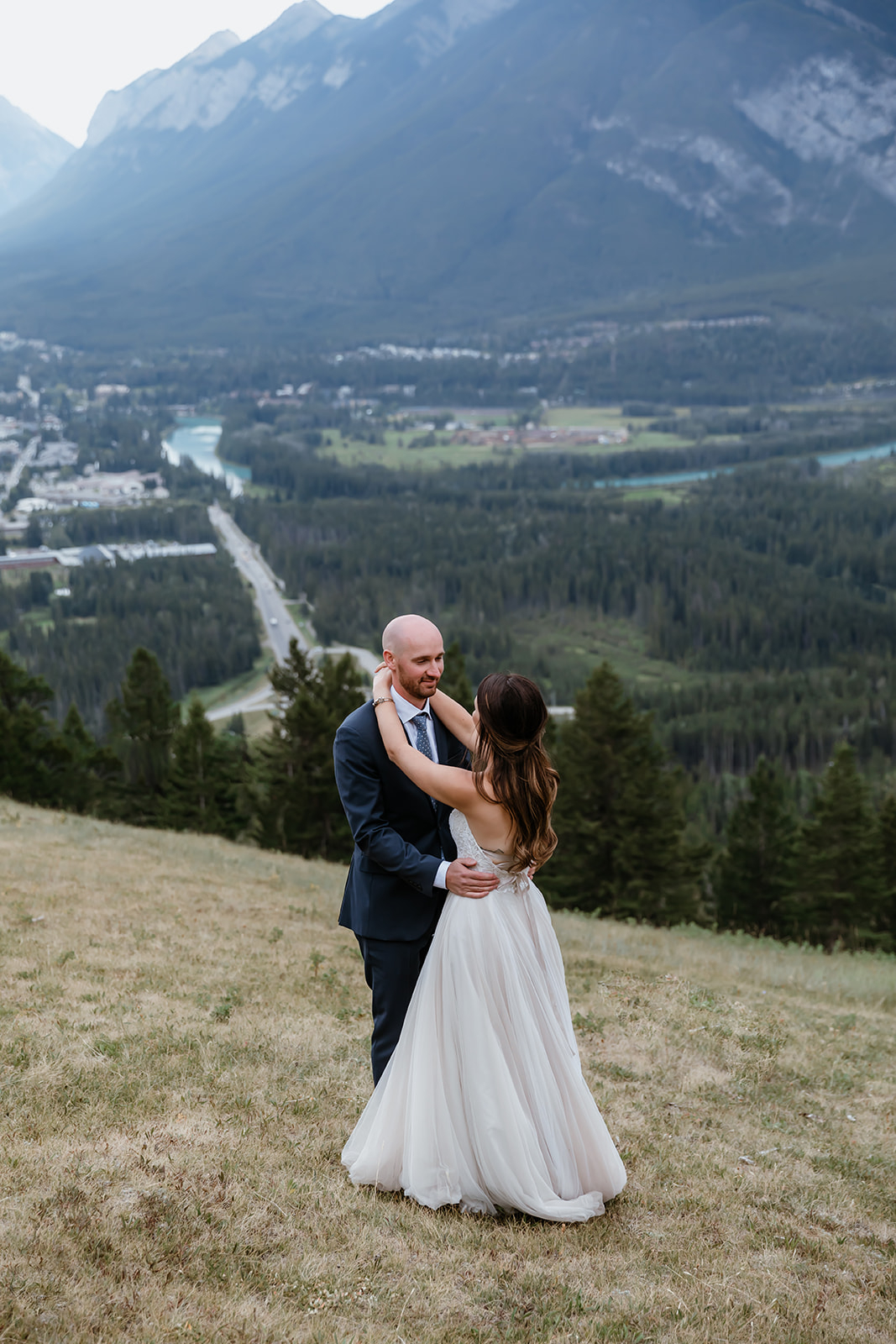 lake-Minnewanka-wedding A couple shares a quiet moment on a mountainside, overlooking the town of Banff below, after their Lake Minnewanka Wedding