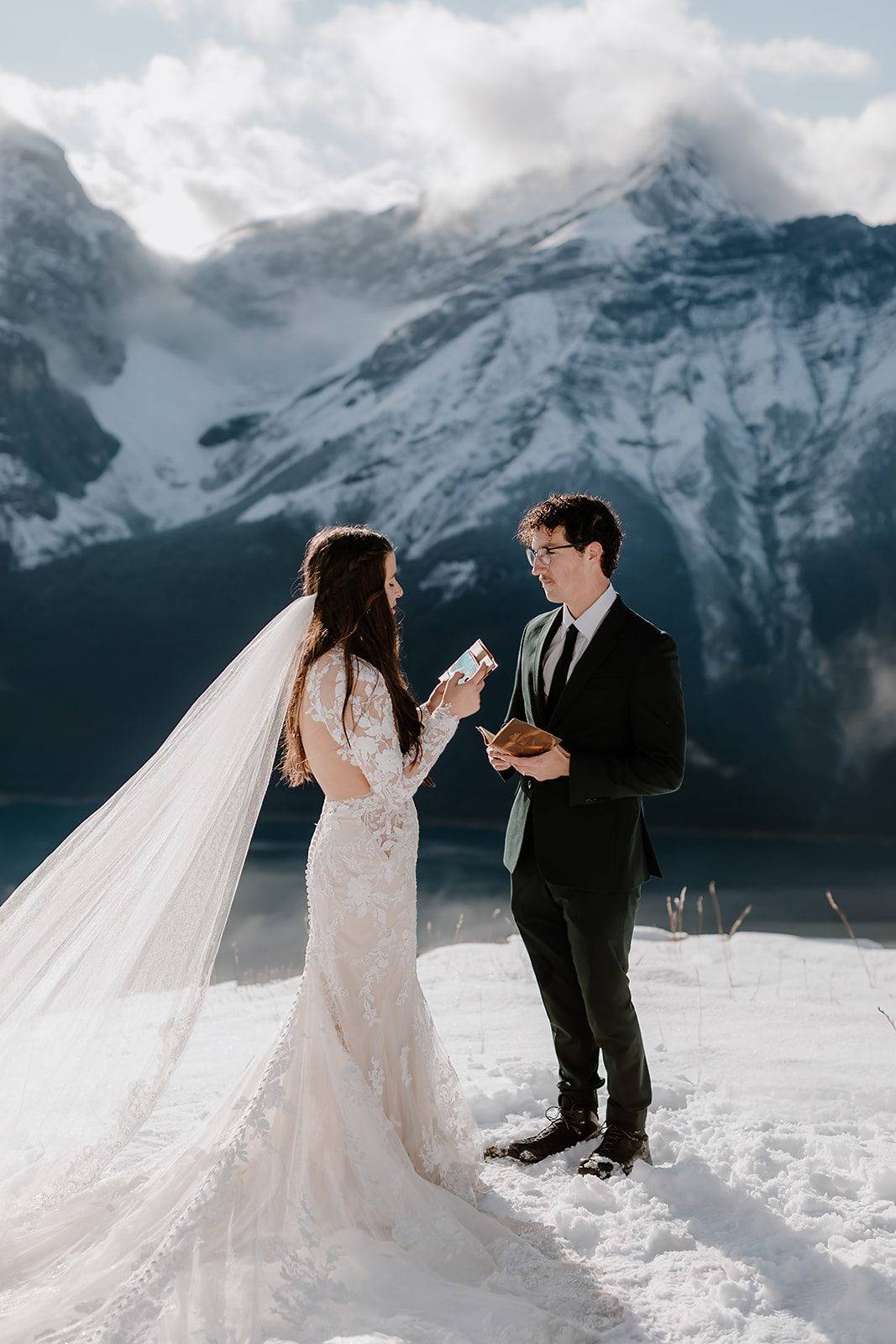 Couple exchanging vows during their winter hiking elopement in Banff, standing in the snow with dramatic mountain peaks behind them.