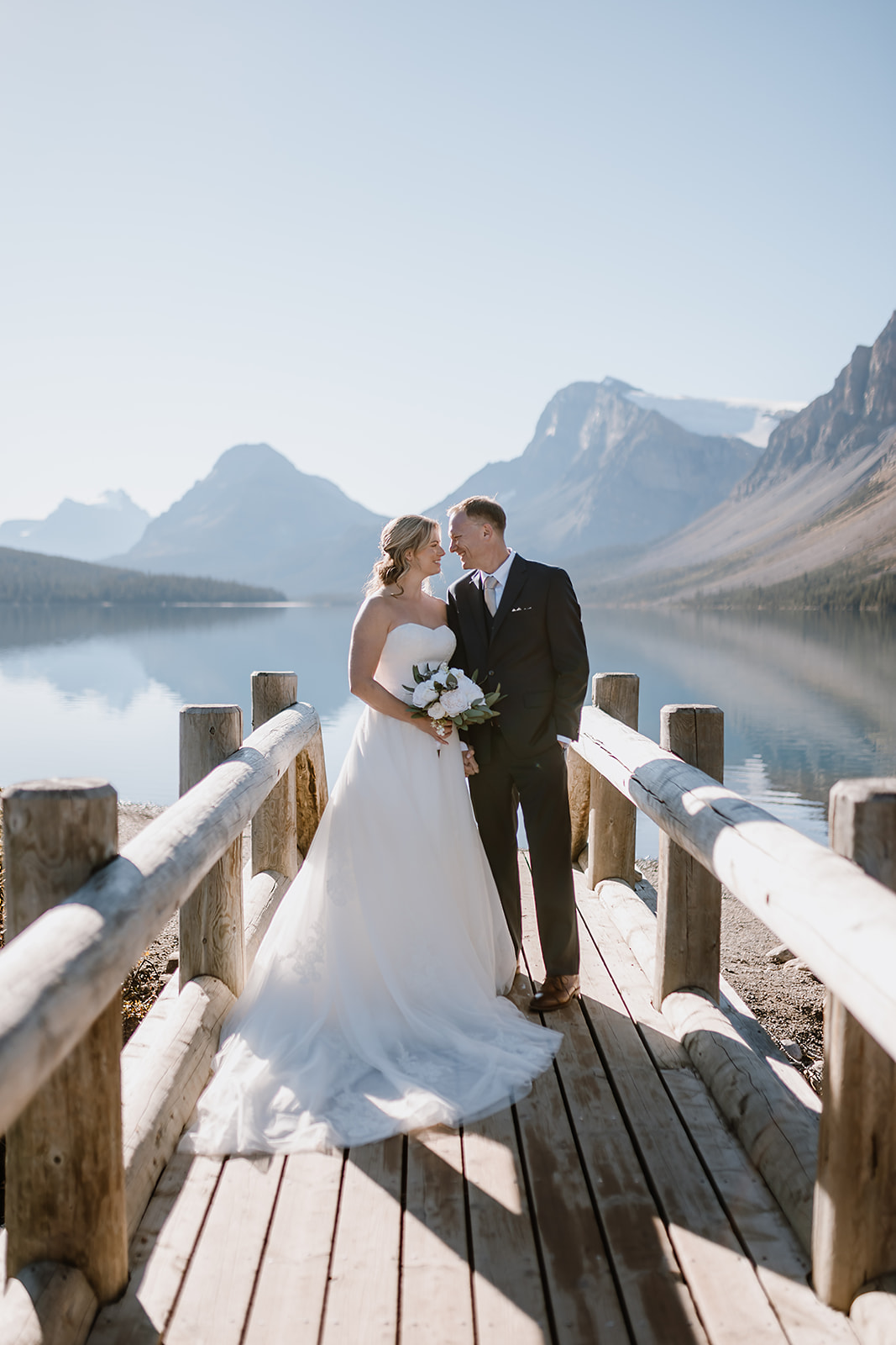 Bride and groom sharing a quiet moment on a wooden bridge during their hiking elopement in Banff, surrounded by still water and mountain reflections.